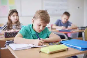 Schoolboy writing in exercise book in class