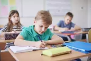 Schoolboy writing in exercise book in class